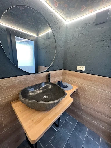 Baño compacto con bañera y revestimiento cerámico, detalles en madera y espejo iluminado.
